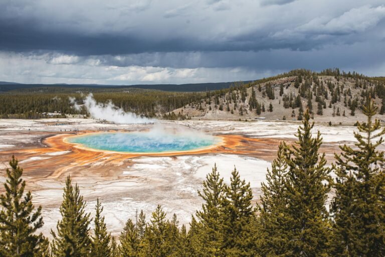 A breathtaking view of the Grand Prismatic Spring in Yellowstone National Park with vibrant colors and a cloudy sky.