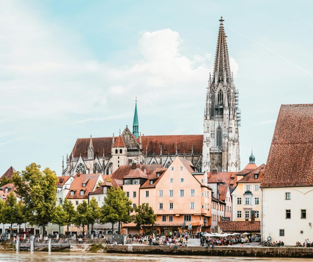 Picturesque view of Regensburg Cathedral with colorful houses and serene riverfront in Germany.