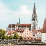 Picturesque view of Regensburg Cathedral with colorful houses and serene riverfront in Germany.