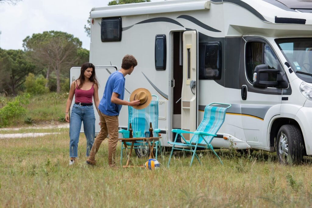 Outdoor scene of a young couple setting up camp next to their RV during a summer day in Portugal.