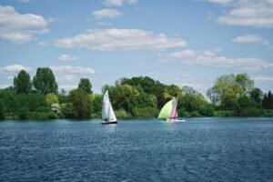 A serene view of sailboats on a lake surrounded by lush greenery under a vibrant blue sky in Gütersloh, Germany.