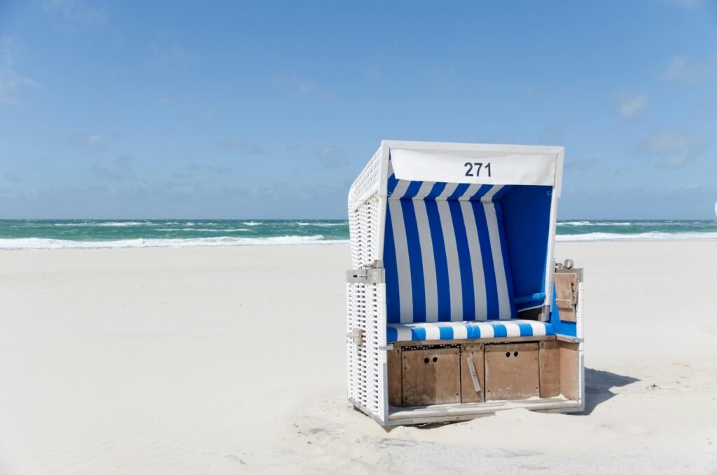 A striped beach chair on the sandy shores of Sylt, Germany under clear blue skies.