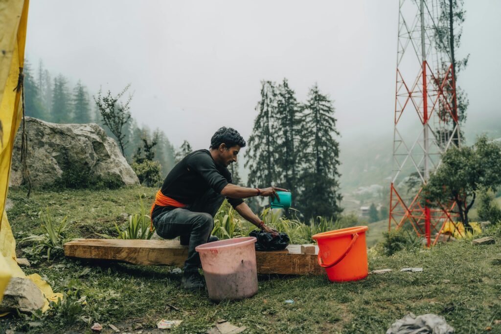 A man washes clothes outdoors in a rural area with misty trees and a utility tower in the background. ß Wohnmobil Waschmaschine