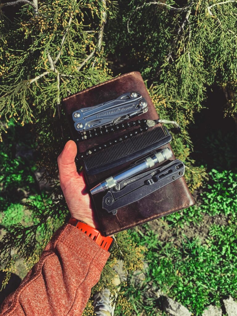 A person holding a leather case with - Camping-Zubehör multitools amidst lush green foliage, showcasing adventure readiness.