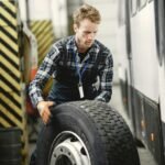 Auto mechanic working indoors in a vehicle repair garage managing a large tire.