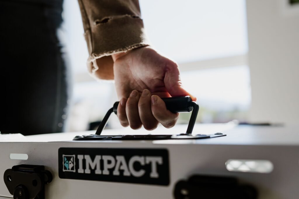 Close-up of a hand gripping an Impact dog crate handle indoors.