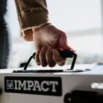 Close-up of a hand gripping an Impact dog crate handle indoors.