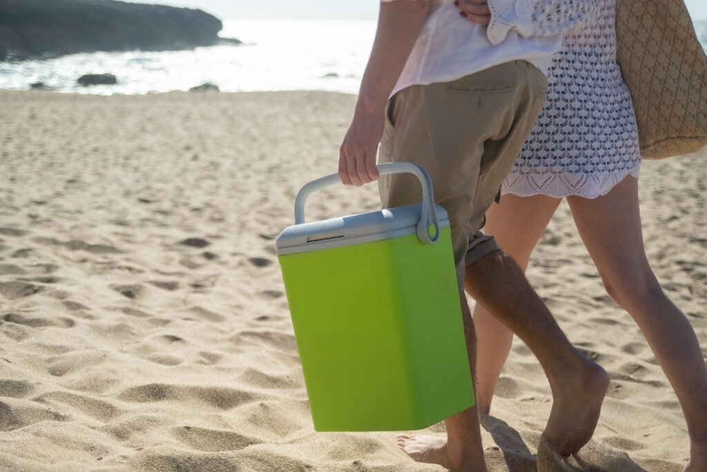 A couple walks along a sunny beach in Portugal carrying a cooler.
