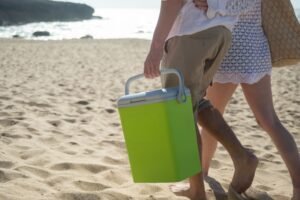 A couple walks along a sunny beach in Portugal carrying a cooler.