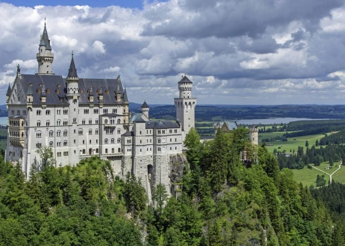 Stunning view of Neuschwanstein Castle surrounded by lush green forests and clouds. Stunning view of Neuschwanstein Castle surrounded by lush green forests and clouds.