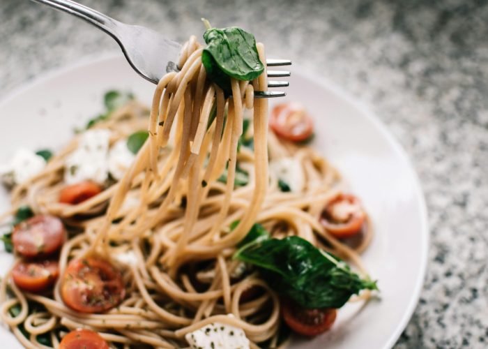 Delicious whole wheat pasta with fresh spinach, cherry tomatoes, and feta cheese in a close-up shot. Delicious whole wheat pasta with fresh spinach, cherry tomatoes, and feta cheese in a close-up shot.