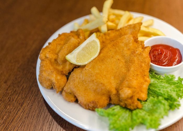 Delicious schnitzel served with fries, lettuce, lemon, and ketchup on a wooden table. Delicious schnitzel served with fries, lettuce, lemon, and ketchup on a wooden table.