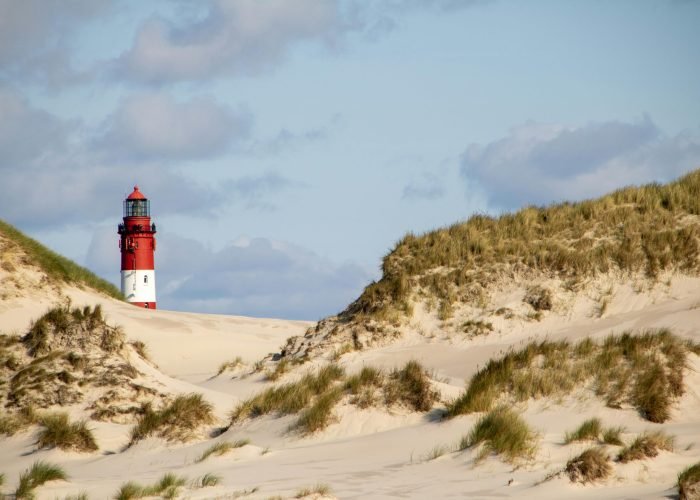 Red and white lighthouse surrounded by sandy dunes under a partly cloudy sky on Amrum Island. Red and white lighthouse surrounded by sandy dunes under a partly cloudy sky on Amrum Island.