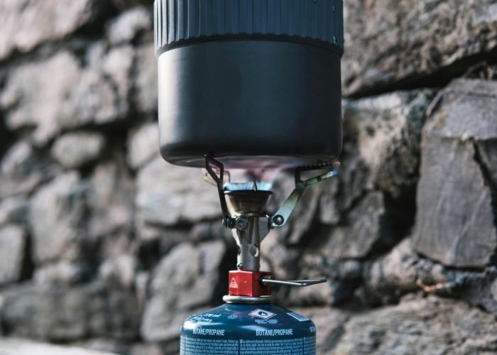 pexels-photo-31478478-31478478 Portable camping stove on a wooden surface with stone wall background in Espelette, France.