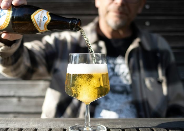Adult pouring beer into a glass outside on a sunny day, featuring a clear, refreshing drink.