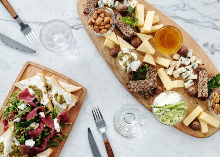 A top view of assorted cheeses, nuts, meats, and bread on a wooden charcuterie board. A top view of assorted cheeses, nuts, meats, and bread on a wooden charcuterie board.