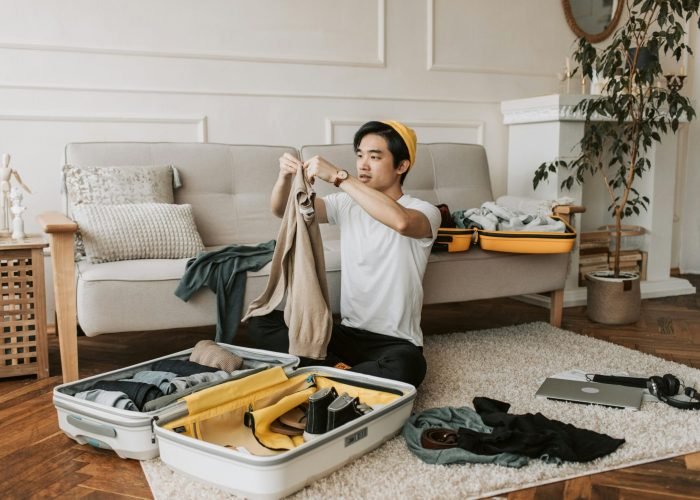 A young man organizes clothes into a suitcase in a stylish living room, preparing for a trip. A young man organizes clothes into a suitcase in a stylish living room, preparing for a trip.