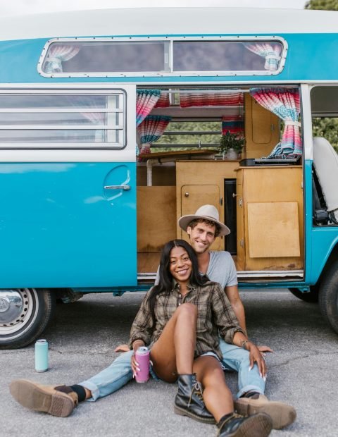 Wohnmobil oder Wohnwagen? Entdecke, welches Fahrzeug besser zu deinem Reise- und Lebensstil an der Mosel passt! Happy couple sitting by classic van enjoying a sunny day outdoors. Embrace the van life spirit.