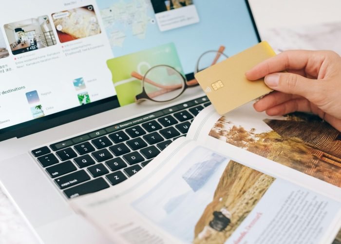 pexels-photo-8937451-8937451 Hands holding credit card over laptop and magazine for online shopping and travel planning.