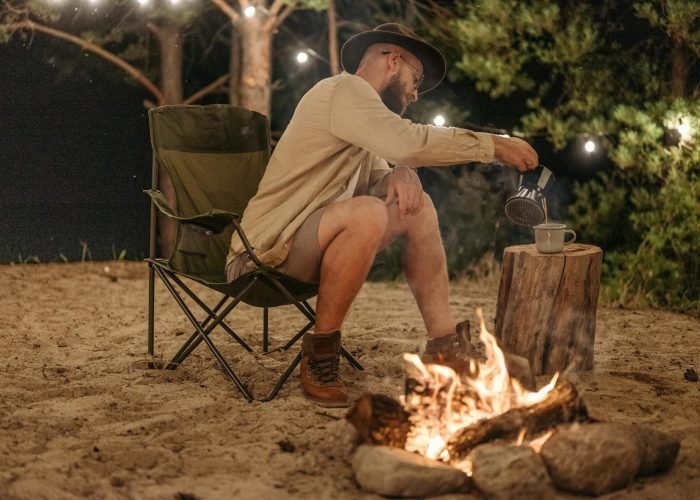 pexels-photo-9143907-9143907 A man pours coffee over a campfire at a camping site during the night.