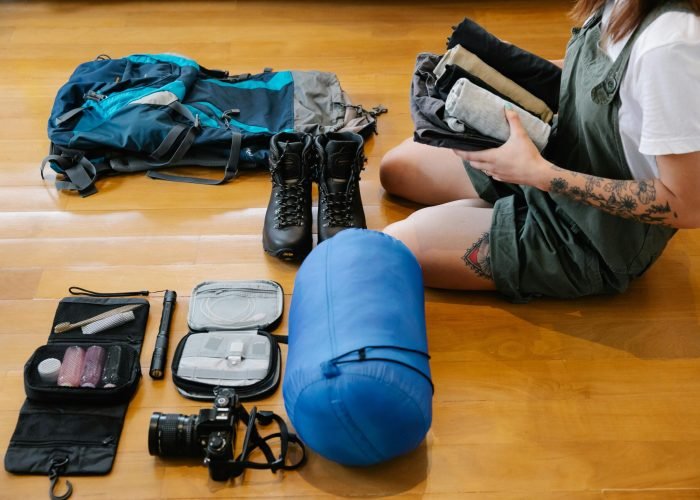 pexels-photo-9186048-9186048-1 Woman organizing camping gear and clothes on wooden floor indoors, preparing for an adventure.